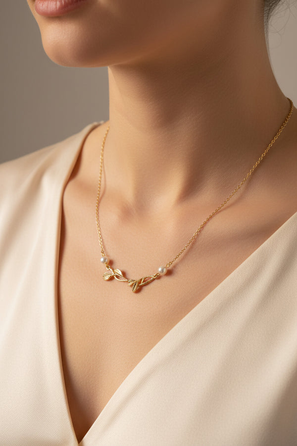 Gold necklace with leaf and pearl details on a light blue background
